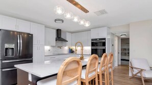 A modern kitchen with white cabinets, a stainless steel refrigerator, a central island with bar stools, and pendant lighting. - Island Vibes - 3BR Pool Home near St. Pete Beach (St. Petersburg)