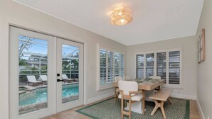 A room with a pool view, a dining area with a table and chairs, and large windows. - Island Vibes - 3BR Pool Home near St. Pete Beach (St. Petersburg)