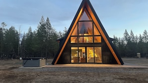 En moderne, trekantet træhytte med store glasruder, et synligt køkkenområde og en grusvej.