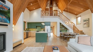 En rummelig opholdsstue med højt til loftet, træbjælker, en central ø og en trappe til en etage ovenover.