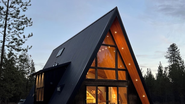 En moderne hytte med en trekantet form, store vinduer og en træfacade.