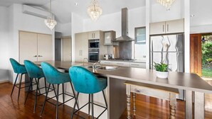 Una cocina moderna con una isla central, taburetes de bar, electrodomésticos de acero inoxidable e iluminación colgante.