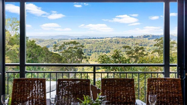 Un comedor con sillas de mimbre y una mesa, con vistas a un paisaje pintoresco con árboles y colinas.