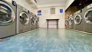 A laundry facility with multiple washing machines, a tiled floor, and a notice sign on the wall.