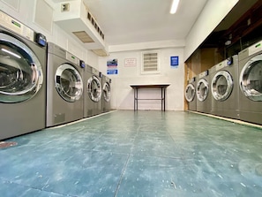 Un cuarto de lavandería con varias lavadoras, piso de baldosas y un cartel en la pared.
