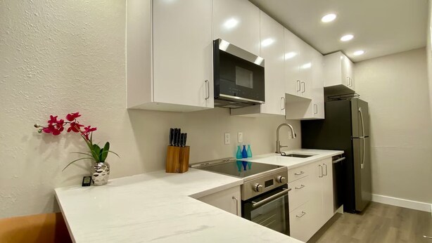 A modern kitchen with white cabinets, a black refrigerator, a microwave, and an oven. There is a vase with flowers on the counter.