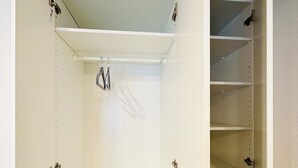 A walk-in closet with open doors, featuring metal shelves, a hanging rod, and a metal rack at the bottom.