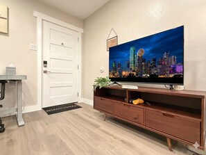 Un salon avec un téléviseur à écran plat fixé à un meuble de rangement en bois, une porte et un petit bureau avec une chaise.