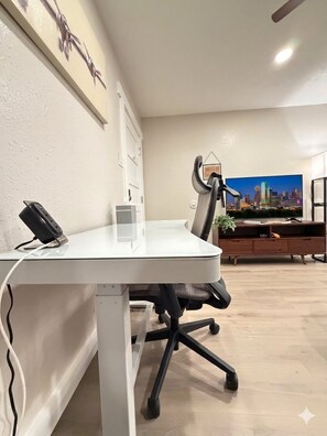 Un espacio de oficina moderno con un escritorio blanco, una silla de oficina negra y un televisor que muestra un paisaje urbano.