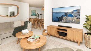 Uma sala de estar moderna com um sofá, duas mesas redondas de madeira, uma televisão e uma estante de livros.
