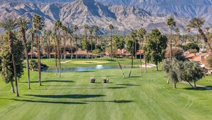 A golf course with a pond, palm trees, and mountains in the background. - Palm Desert Golf Course Condo w/ Patio Views, Fireplace, Resort Pool & Mountain Backdrop (Palm Desert)