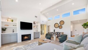 A spacious living room with a fireplace, a flat-screen TV mounted on the wall, and a dining area with a table and chairs. - Palm Desert Golf Course Condo w/ Patio Views, Fireplace, Resort Pool & Mountain Backdrop (Palm Desert)