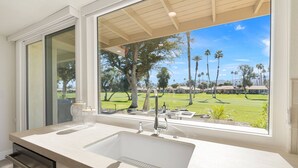 A modern bathroom with a large window, a double sink, and a view of a golf course. - Palm Desert Golf Course Condo w/ Patio Views, Fireplace, Resort Pool & Mountain Backdrop (Palm Desert)