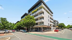 Ett hotell med flera våningar, balkonger, ett takförsett utomhusområde och utsikt över gatan med parkerade bilar.