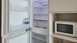 Un refrigerador abierto con varias estantes y un microondas a la derecha.