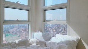 Un dormitorio con cama, dos ventanas y vistas a la ciudad.