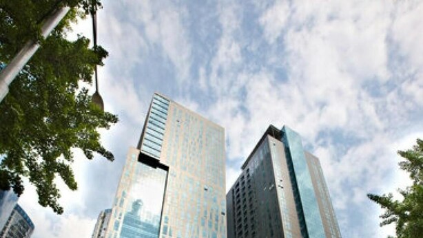 Un edificio moderno de gran altura con fachada de vidrio, rodeado de un paso de peatones y farolas.