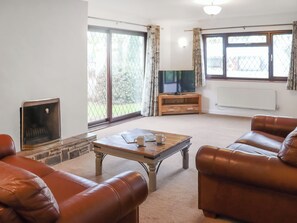 Una sala de estar con sofás de cuero, una mesa de centro, chimenea, televisor y ventanas grandes con cortinas.