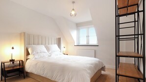 A bedroom with a bed, two bedside tables, a radiator, a window, and a wooden shelf. - Stylish modern home with games room, luxury kitchen and two en suite bedrooms. (Ross-on-Wye)