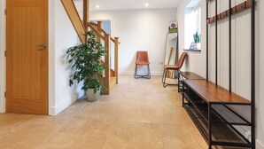 A hallway with a wooden door, a staircase, a potted plant, two chairs, a mirror, and a metal shelf unit. - Stylish modern home with games room, luxury kitchen and two en suite bedrooms. (Ross-on-Wye)