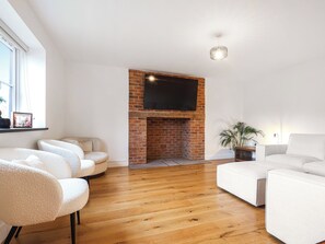 A living room with a brick fireplace, white sofas, and a flat-screen TV mounted above it. - Stylish modern home with games room, luxury kitchen and two en suite bedrooms. (Ross-on-Wye)