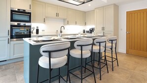 A modern kitchen with a central island, bar stools, built-in ovens, and a skylight. - Stylish modern home with games room, luxury kitchen and two en suite bedrooms. (Ross-on-Wye)