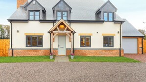 A two-story house with a gabled roof, a front porch with a triangular wooden frame, and a garage on the right. - Stylish modern home with games room, luxury kitchen and two en suite bedrooms. (Ross-on-Wye)