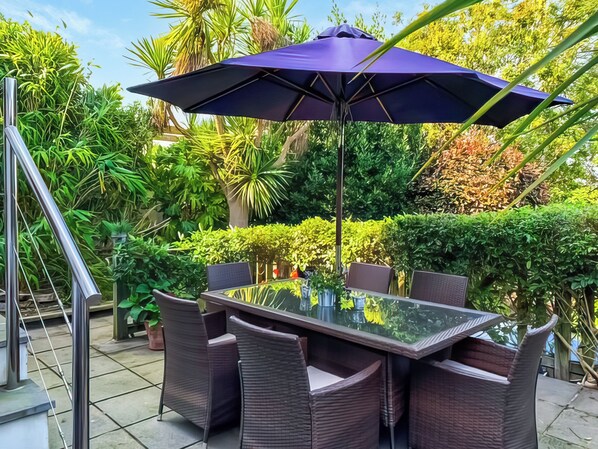 Une table à plateau en verre, six chaises en osier et un parasol violet.