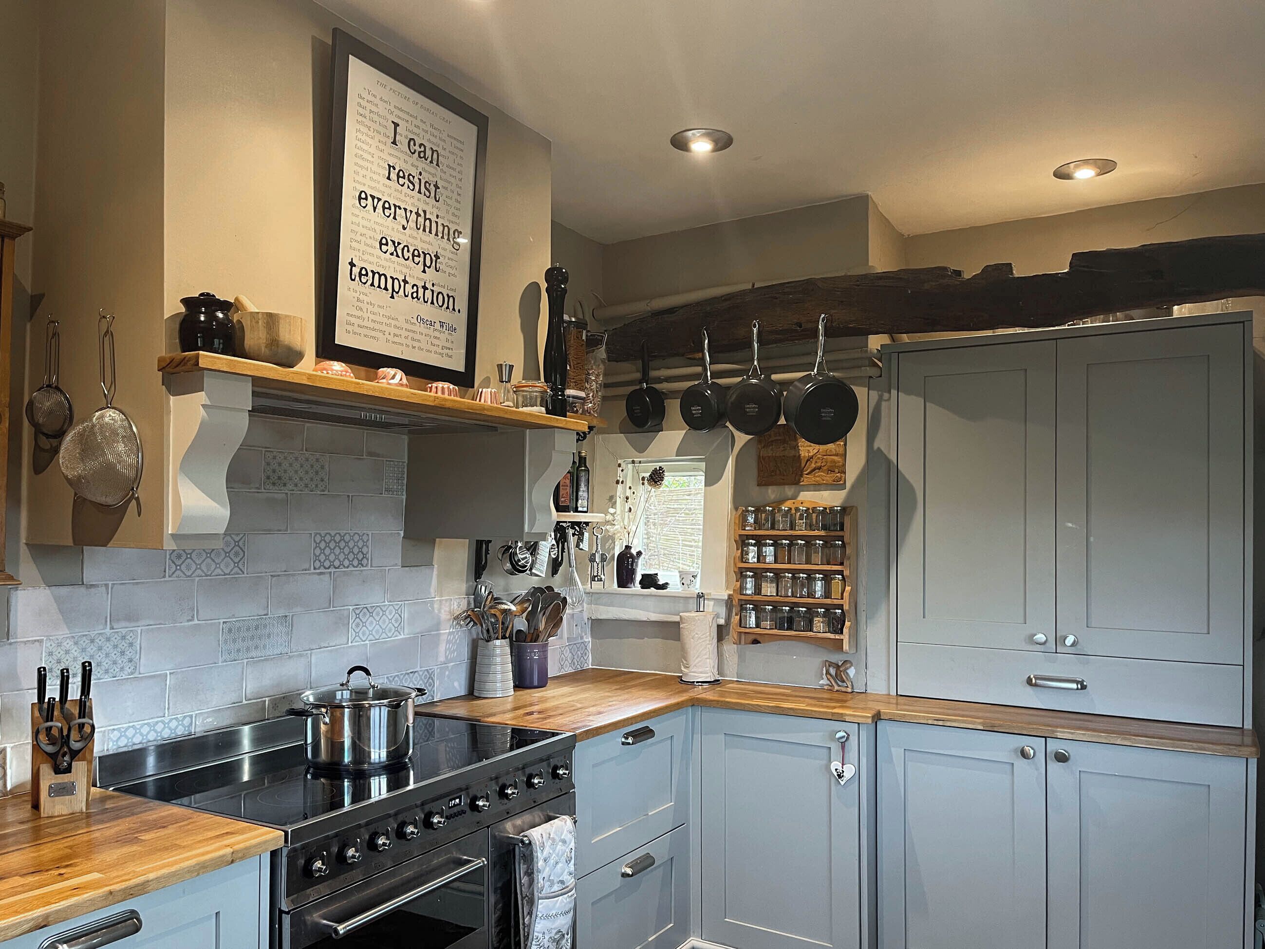 A kitchen with a stove, oven, and various utensils. There is a shelf with pots and pans, and a wall-mounted rack with more pots.