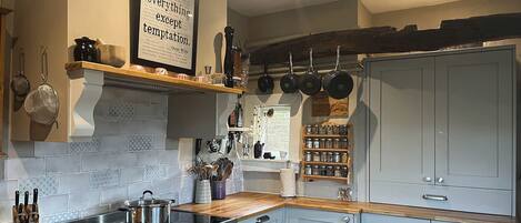 A kitchen with a stove, oven, and various utensils. There is a shelf with pots and pans, and a wall-mounted rack with more pots.