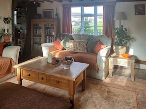 A cozy living room with a sofa, a wooden coffee table, a bookshelf, and a view of the outside.