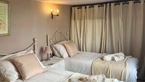 Ein Schlafzimmer mit zwei Betten, beigen Vorhängen, einer Wandleuchte und einem gerahmten Bild.