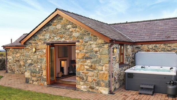 A stone building with a hot tub and a door leading inside. - Beudy Newydd - UK50959 (Llanllechid, near Bangor)