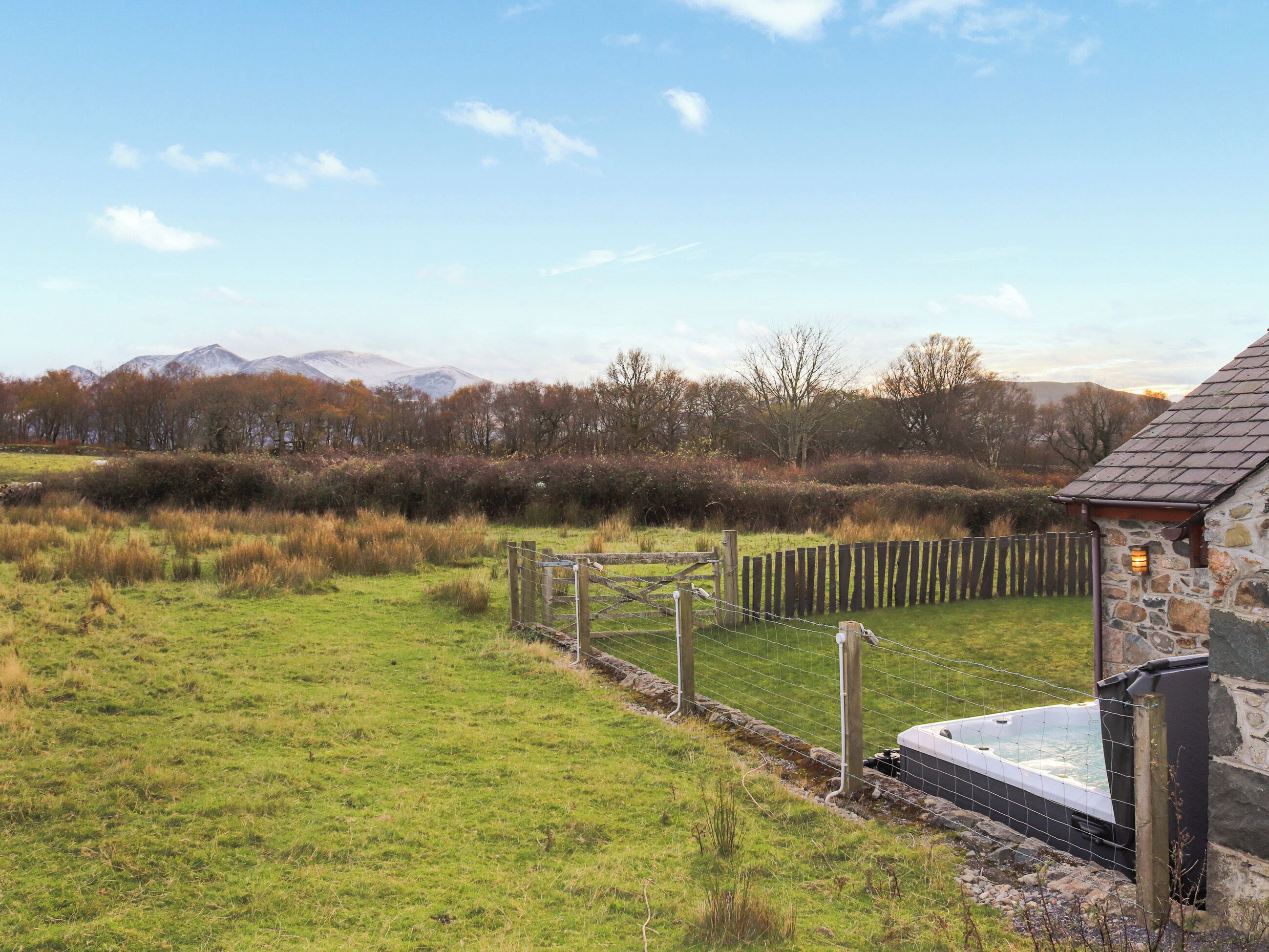 A stone building with a metal gate, a grassy field, and mountains in the background.