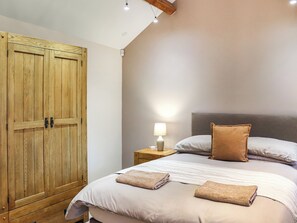 Une chambre avec une grande armoire en bois, une table de chevet avec une lampe, un lit avec des oreillers et une couverture, et une tête de lit.