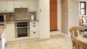 A kitchen with white cabinets, a microwave, a stove, and a wooden ceiling. - Beudy Newydd - UK50959 (Llanllechid, near Bangor)