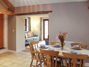 Un coin repas avec une table dressée pour quatre personnes, entourée de chaises en bois. On aperçoit un canapé et une lampe au fond.