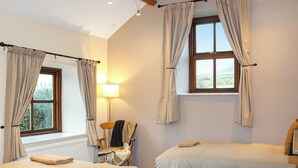 A bedroom with two beds, a lamp, a chair, and a window with curtains. - Beudy Newydd - UK50959 (Llanllechid, near Bangor)