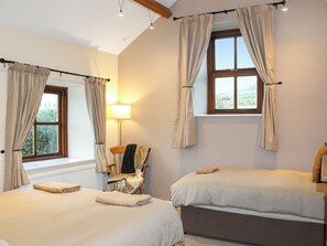 Une chambre avec deux lits, une lampe, une chaise et une fenêtre avec des rideaux.