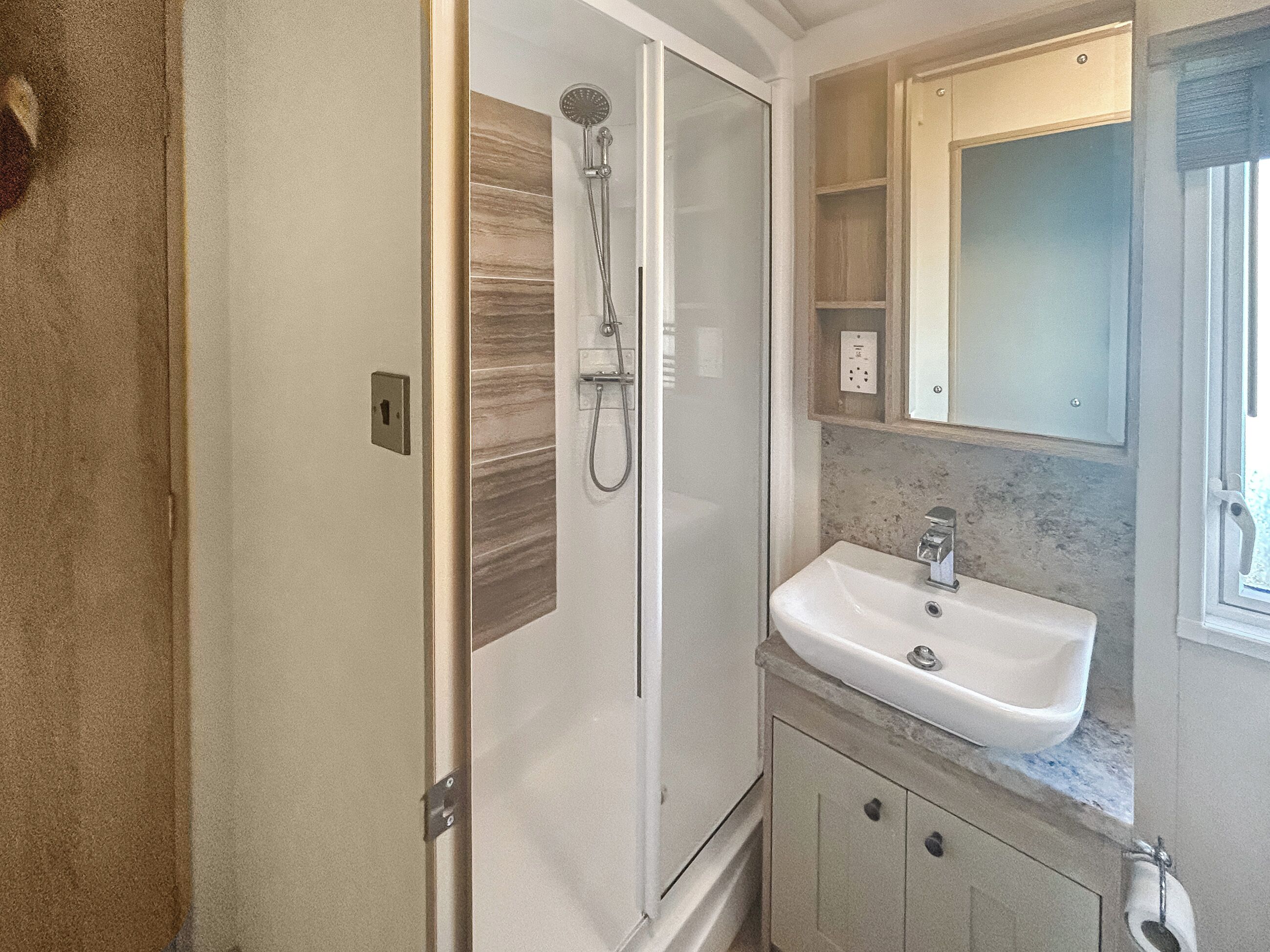 Une salle de bain dotée d’une douche à parois de verre, d’un lavabo blanc et d’un comptoir en marbre.