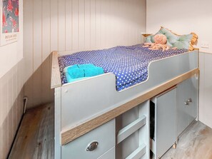 Ein Etagenbett mit blauer Matratze mit Sternenmuster, einer blauen Decke und einem Kuscheltier. Darunter befinden sich zwei Schubladen.