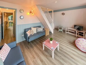 A living room with a blue sofa, a pink table with a plant, a staircase, a TV stand, and a small heater. - A lovely lodge in a great holiday village. (Kingsdown, Deal)