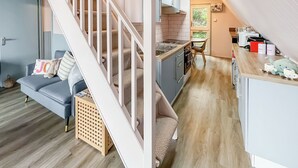 Ein kompakter Wohnraum mit einer Treppe zu einem Erkerbereich, einer Küchenzeile und einer Sitzecke mit Sofa und Kissen.