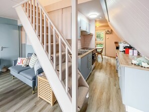 Ein kompakter Wohnraum mit einer Treppe zu einem Erkerbereich, einer Küchenzeile und einer Sitzecke mit Sofa und Kissen.