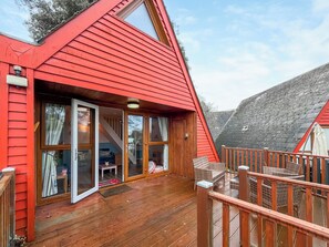 Une cabane au toit rouge, dotée d’une terrasse en bois et d’une porte vitrée donnant sur un escalier.
