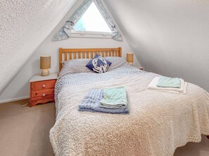 Une chambre confortable avec un plafond en pente, un cadre de lit en bois, une literie à carreaux et une petite table de chevet avec des lampes.