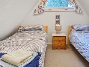 A bedroom with two beds, a nightstand with a lamp, and a window with curtains. - A lovely lodge in a great holiday village. (Kingsdown, Deal)
