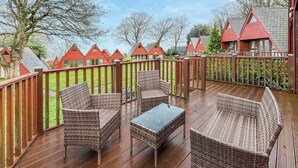 Eine Holzterrasse mit Korbmöbeln und einem Glastisch, umgeben von einem Holzzaun.