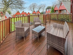 Eine Holzterrasse mit Korbmöbeln und einem Glastisch, umgeben von einem Holzzaun.