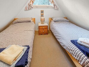 A small, cozy bedroom with two single beds, a nightstand, a lamp, and a window with curtains. - A lovely lodge in a great holiday village. (Kingsdown, Deal)